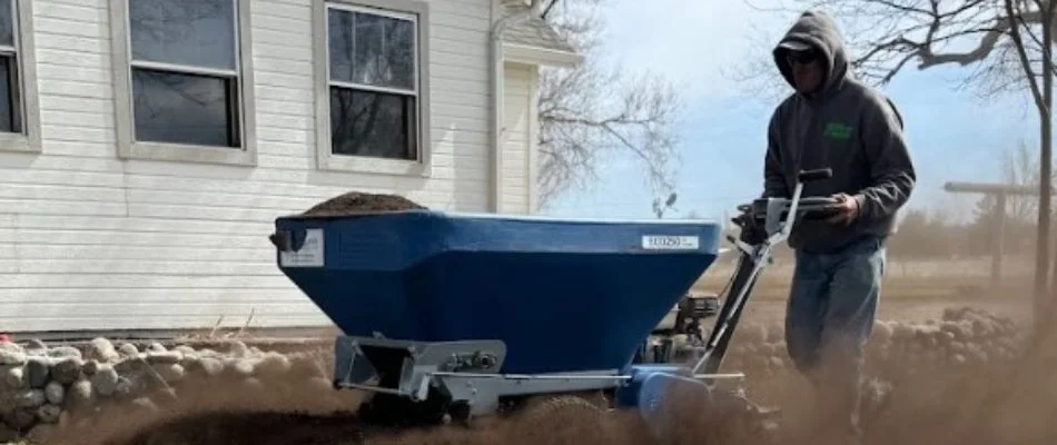 Worker in a hoodie applying topdressing treatment to a lawn in Longmont, CO.